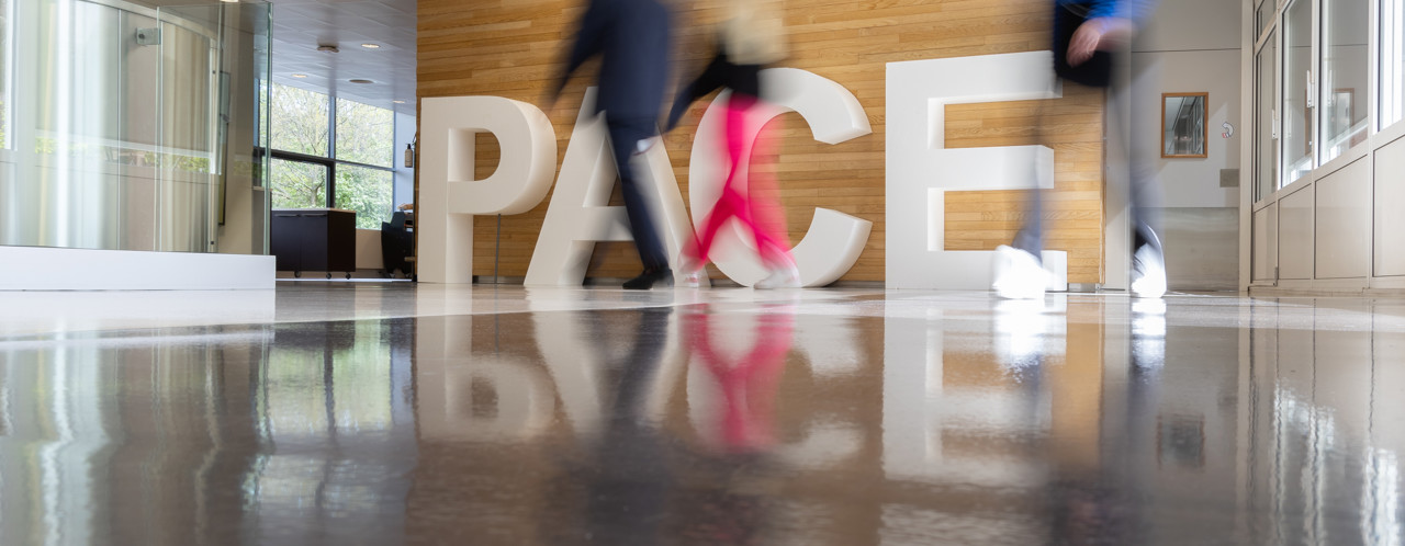 Two people walk beside large letters spelling 'PACE,' reflected on the shiny floor.