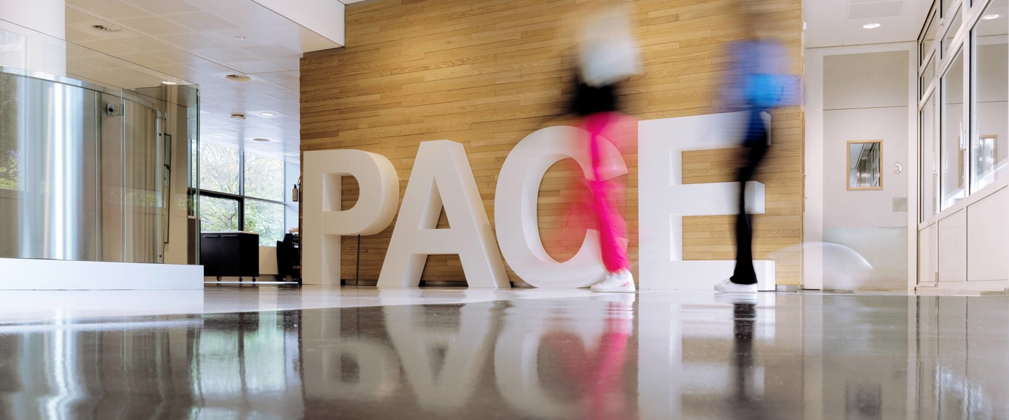 Two people walk past large white letters spelling the word 'PACE' in a modern lobby.