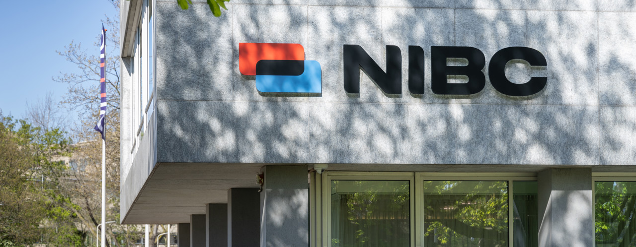 NIBC office with a red and blue logo on a modern facade, surrounded by green trees.