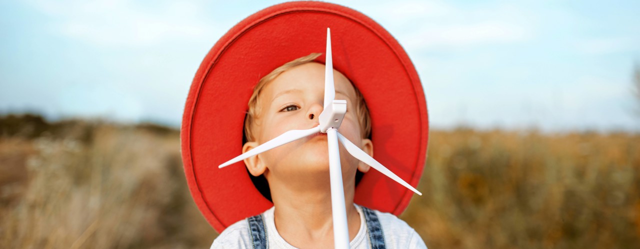 Een kind in een rode hoed staat op een geel grasveld, met een speelse uitstraling en een pijl in de mond.