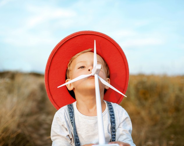 A child in a red hat stands in a field of yellow grass, looking playful with an arrow in its mouth.