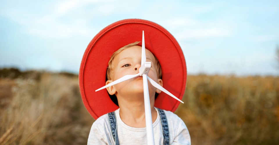 A child in a red hat stands in a field of yellow grass, looking playful with an arrow in its mouth.