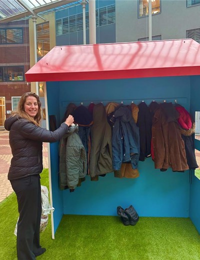 Een persoon hangt een jas op in een kleurrijk garderobehuisje met verschillende jassen aan haken.