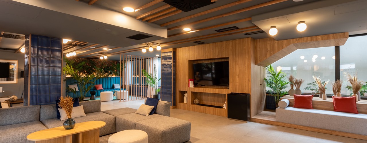 Moderne lounge met gezellige zithoeken, planten en een grote televisie op een houten wand.