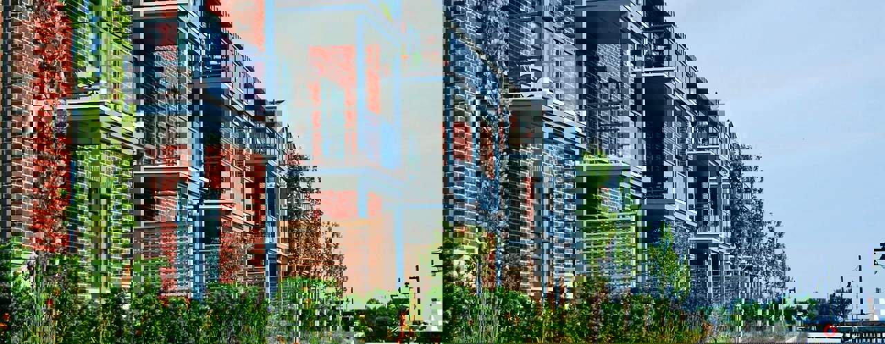 Modern apartment complexes with balconies, surrounded by greenery, along a quiet promenade.