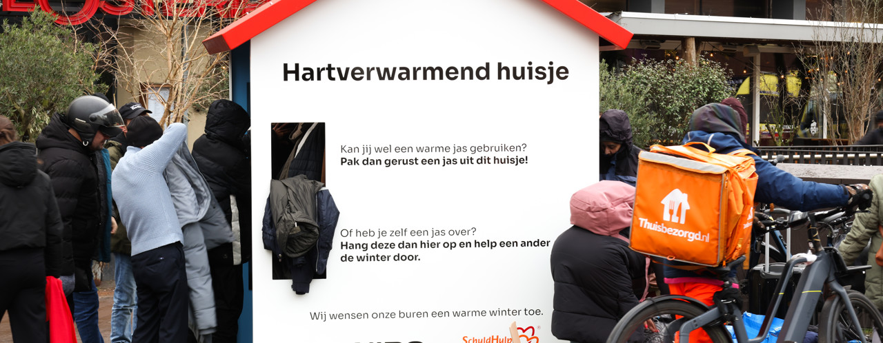 People stand in a line at a wooden kiosk providing information about heat and assistance during the winter.