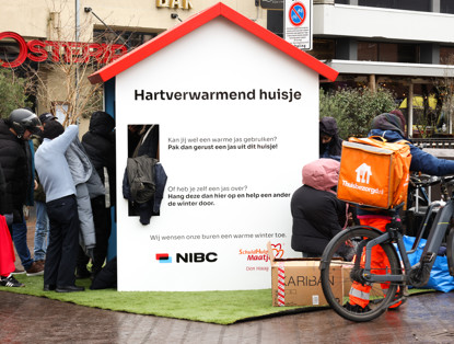 People stand in a line at a wooden kiosk providing information about heat and assistance during the winter.