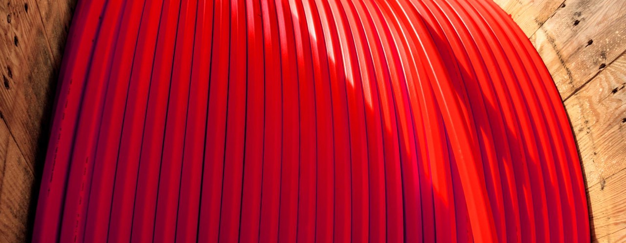 Dikke rode kabel opgerold in een houten houder, klaar voor gebruik in een bouwproject.