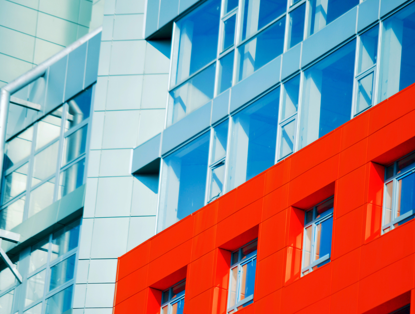 Detail van een gebouw met een felrode gevel en veel glas, wat de moderne architectuur benadrukt.