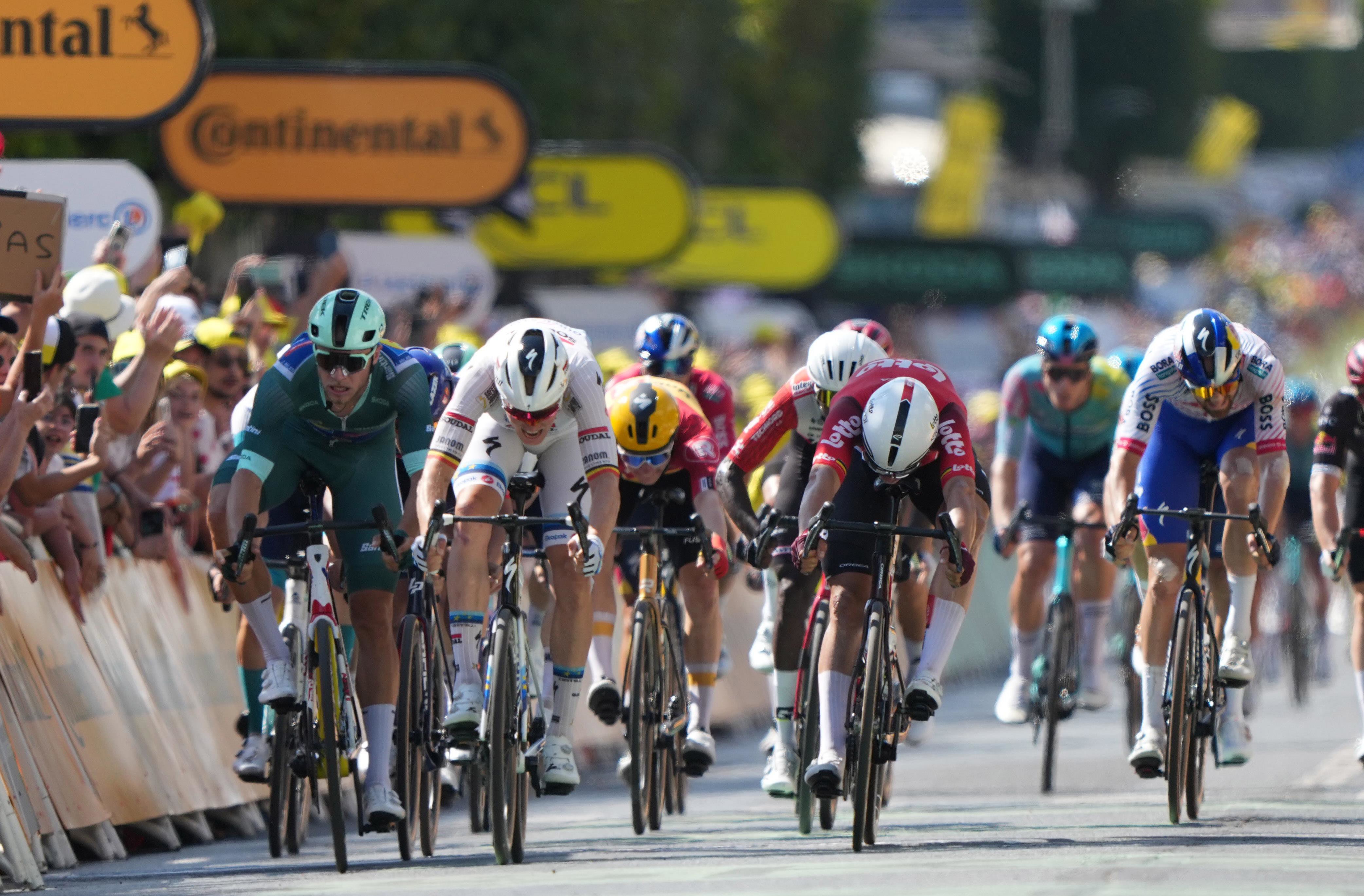 Five cyclists compete in a sprint towards the finish line while the crowd cheers them on with signs.