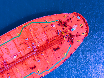 Bovenaanzicht van een groot, felrood vrachtschip met een groene streep en diverse borden op het dek, op een blauwe zee.