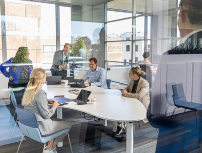 Een groep professionals in een vergaderruimte, gericht op een presentatie met laptops en documenten op tafel.