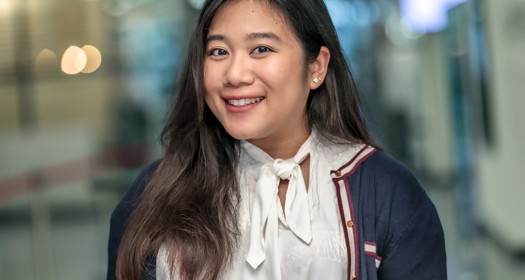 Aranee with long, dark hair and a white blouse is wearing a dark blue sweater with a white bow.