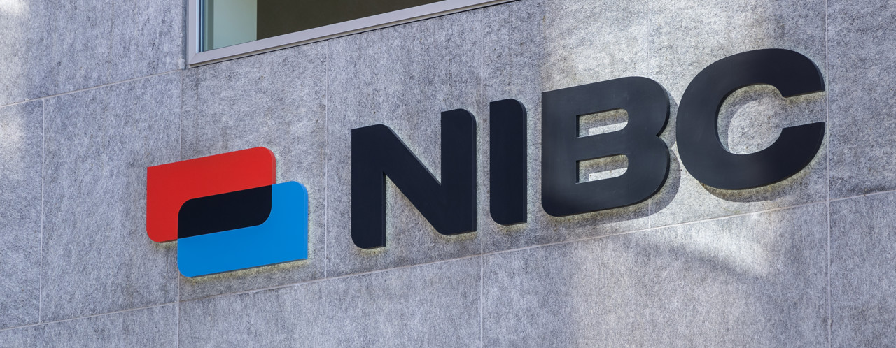 NIBC logo displayed on a gray wall, featuring blue and red elements next to the name in black letters.