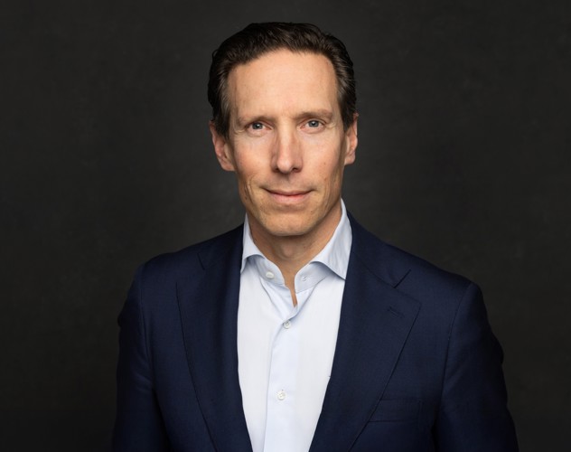 Sven in een donkerblauwe blazer tegen een zwart-grijze achtergrond, met een neutrale blik.