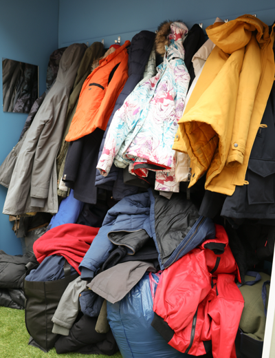 Een stapel kleurrijke jassen en jacks hangt aan haken, terwijl enkele jassen op de grond liggen.