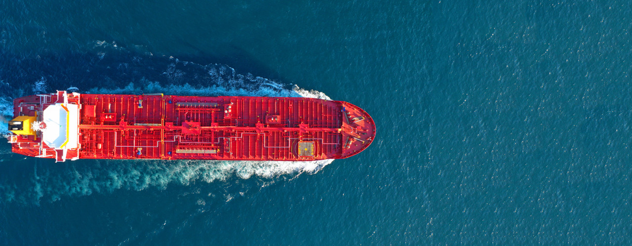 A red cargo ship sails across a blue ocean, its hull reflecting the sunlight.