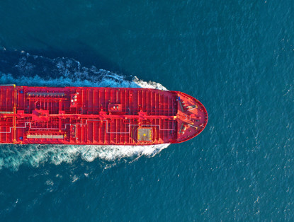 A red cargo ship sails across a blue ocean, its hull reflecting the sunlight.