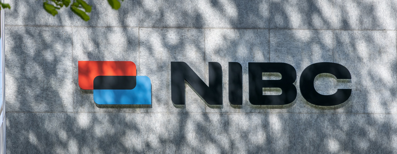 Logo van NIBC met een blauwe en rode blokvorm aan de linkerkant op een grijze achtergrond.