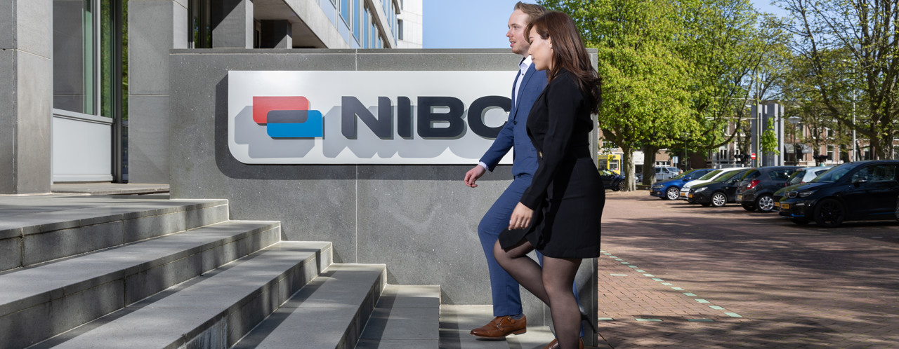 Two people are walking up the stairs to the building with the NIBC logo visible on the facade.