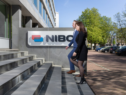 Twee mensen lopen de trap op naar een gebouw met het NIBC-logo op de gevel.