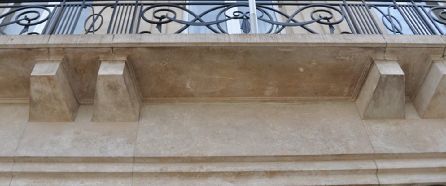 Bovenaan een stenen muur met decoratieve voegen en een zwart ijzeren hek erachter.