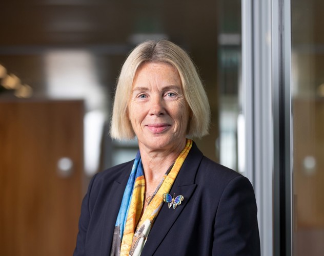 Angelien in business attire wearing a colorful scarf and a butterfly pin, standing in a modern office setting.