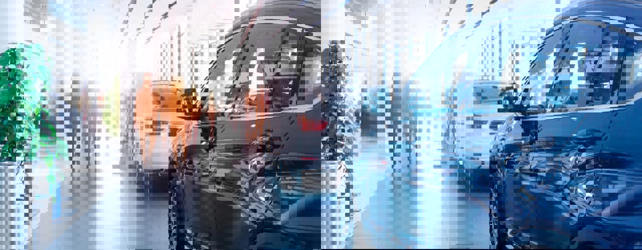 Moderne autobezichtshowroom met een zwarte SUV vooraan en een witte auto op de achtergrond, verlicht door zacht daglicht.