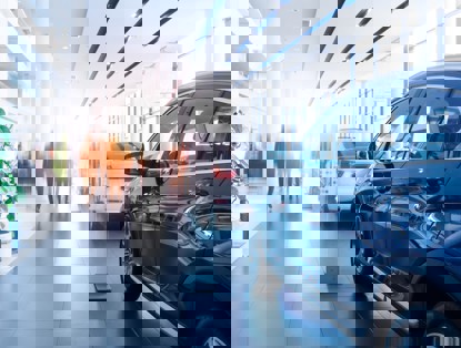 Modern car showroom featuring two cars: a black SUV in the foreground and a white car in the background, illuminated by soft daylight.