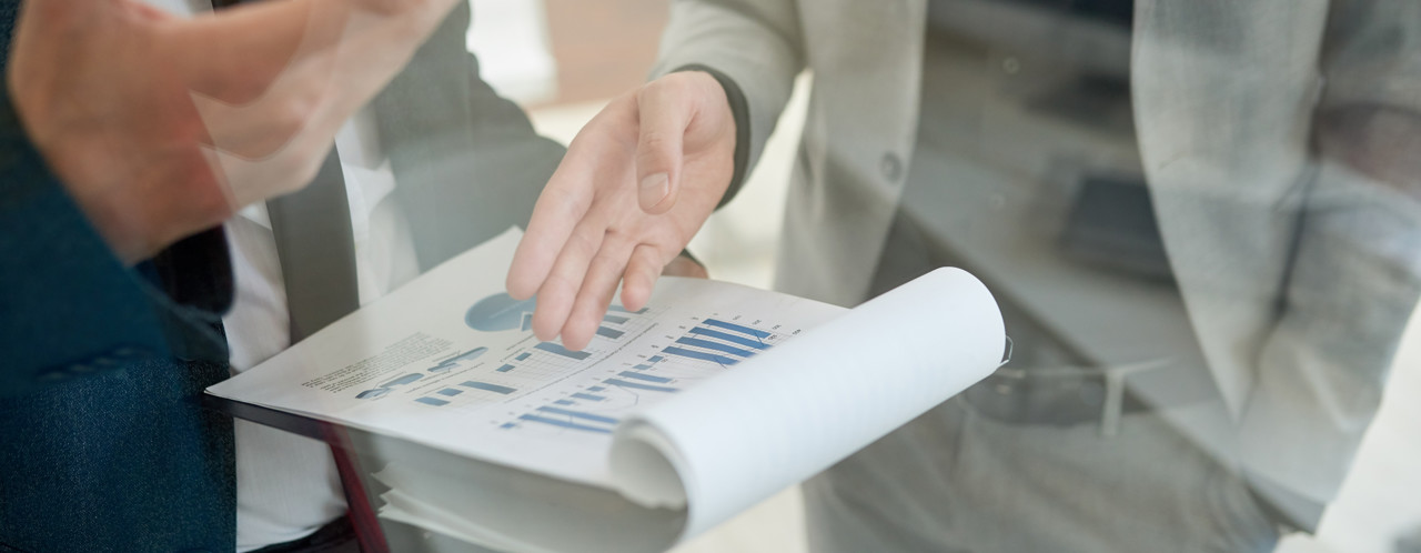 Twee personen bespreken grafieken en cijfers in een document tijdens een vergadering.