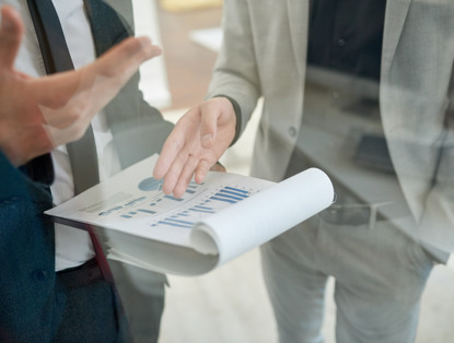 Twee personen bespreken grafieken en cijfers in een document tijdens een vergadering.
