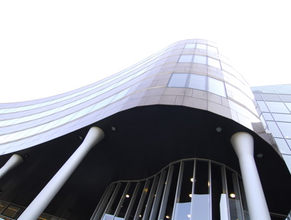 Modern kantoorgebouw met een golvende gevel en grote ramen, ondersteund door witte zuilen.