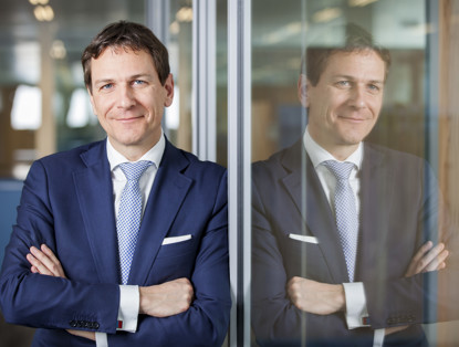 Paulus de wilt with crossed arms stands in front of a glass wall in an office setting.